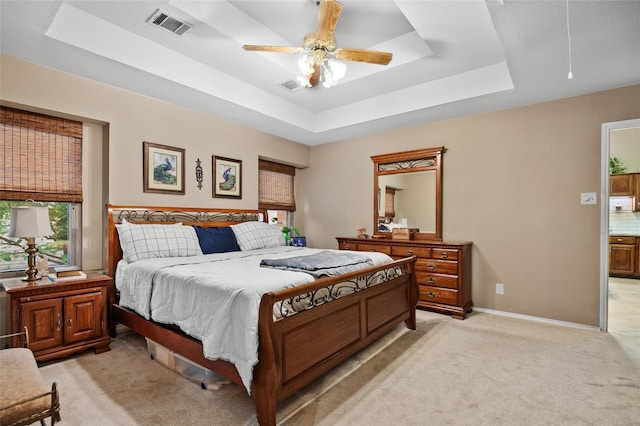 bedroom with a tray ceiling, ceiling fan, and light carpet