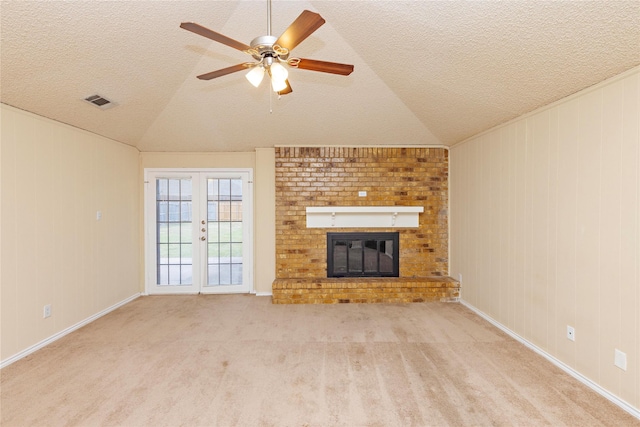 unfurnished living room featuring lofted ceiling, ceiling fan, a fireplace, light colored carpet, and french doors