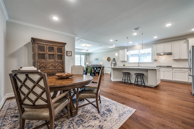 dining area with crown molding, wood-type flooring, and a tray ceiling