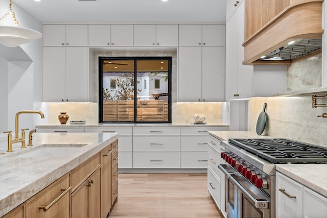 kitchen with double oven range, premium range hood, white cabinetry, and sink