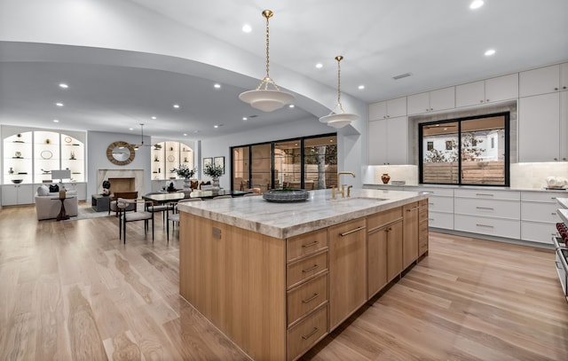 kitchen with decorative light fixtures, white cabinets, a high end fireplace, light stone countertops, and a spacious island