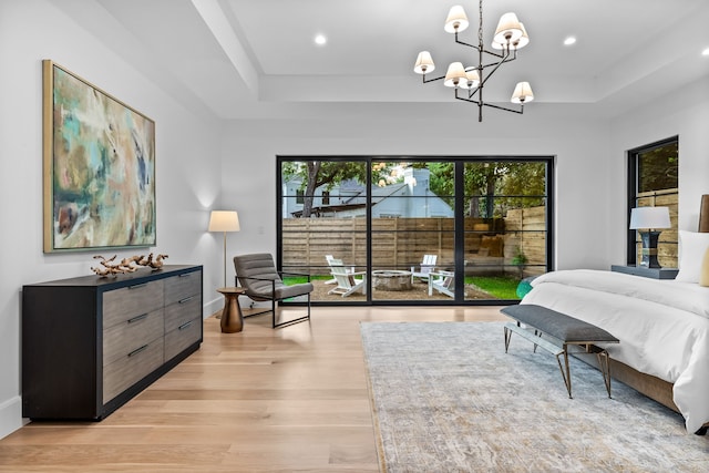 bedroom featuring access to exterior, a raised ceiling, light hardwood / wood-style floors, and a notable chandelier