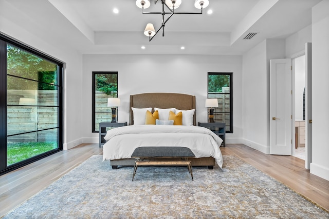 bedroom featuring light wood-type flooring, a tray ceiling, multiple windows, and a notable chandelier