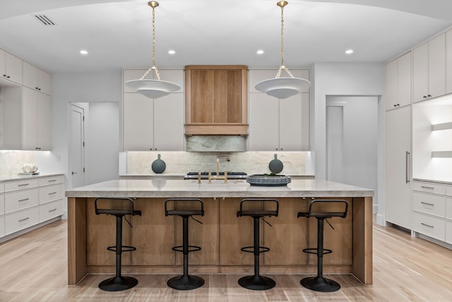 kitchen with a kitchen island with sink, backsplash, decorative light fixtures, and white cabinetry