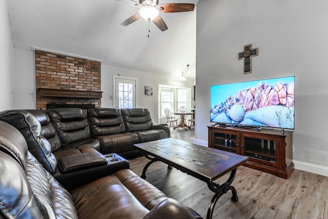 living room featuring a brick fireplace, high vaulted ceiling, ceiling fan, and light wood-type flooring