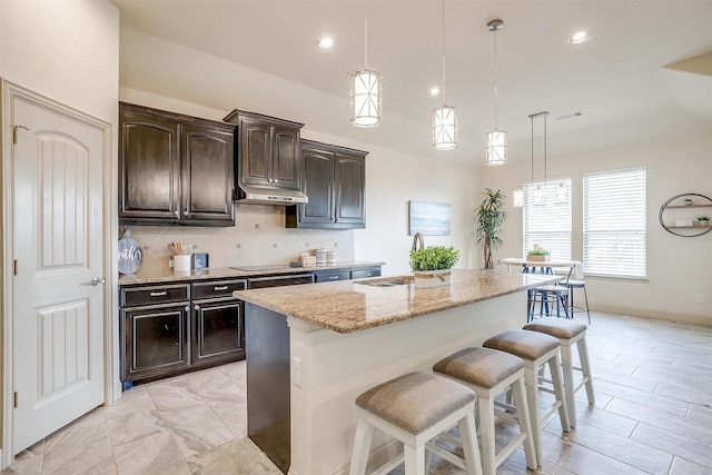 kitchen featuring a kitchen bar, sink, dark brown cabinets, hanging light fixtures, and a kitchen island