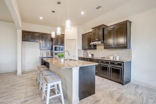 kitchen featuring sink, dark brown cabinets, an island with sink, stainless steel appliances, and light stone countertops