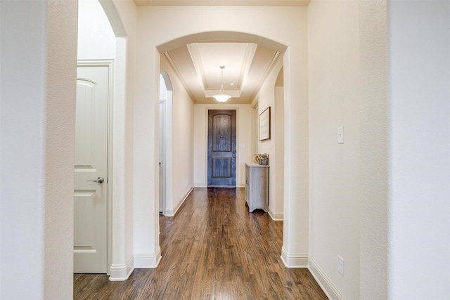 corridor with ornamental molding, dark hardwood / wood-style floors, and a raised ceiling