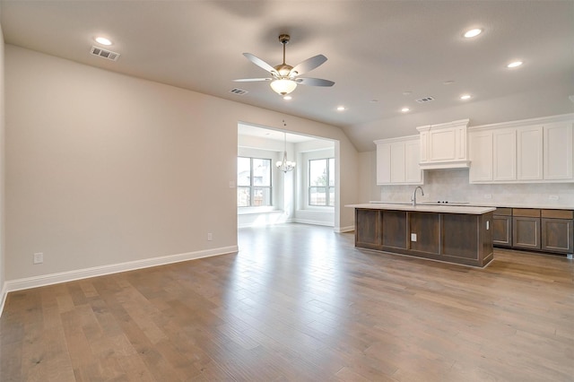 kitchen featuring decorative backsplash, an island with sink, ceiling fan with notable chandelier, and hardwood / wood-style flooring