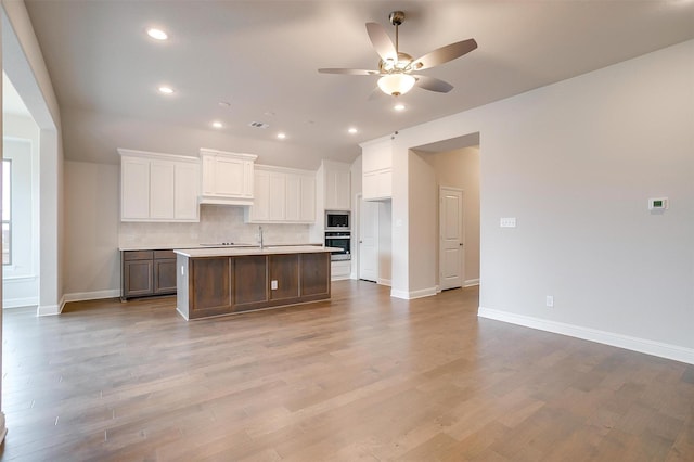 kitchen featuring oven, white cabinets, backsplash, and a kitchen island with sink