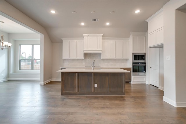 kitchen featuring stainless steel oven, white cabinets, a kitchen island with sink, and built in microwave