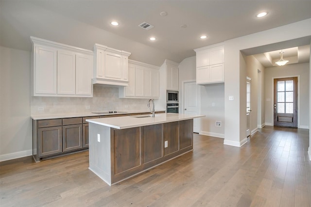 kitchen featuring decorative backsplash, sink, white cabinetry, a kitchen island with sink, and appliances with stainless steel finishes