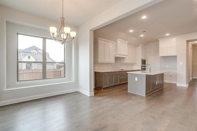 kitchen with an inviting chandelier, white cabinetry, hanging light fixtures, a kitchen island with sink, and stainless steel appliances