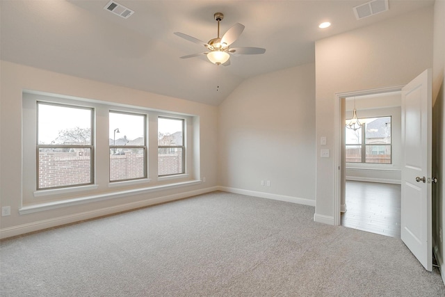 carpeted empty room featuring ceiling fan with notable chandelier and vaulted ceiling