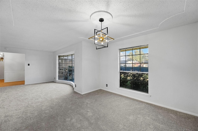 spare room featuring an inviting chandelier, carpet floors, and a textured ceiling