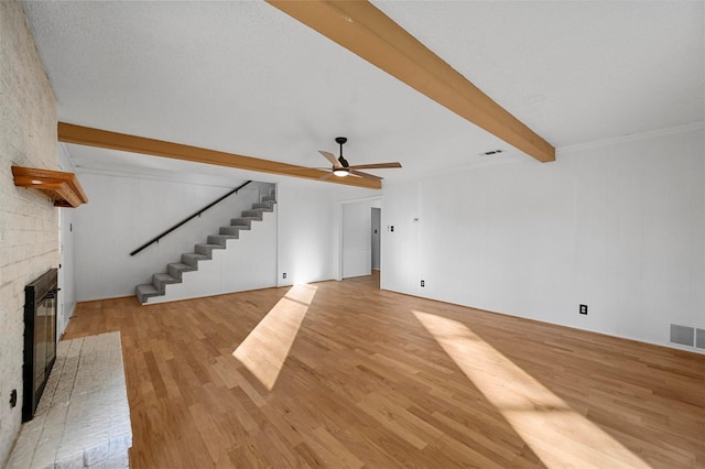 unfurnished living room with ceiling fan, a brick fireplace, beam ceiling, and light hardwood / wood-style floors