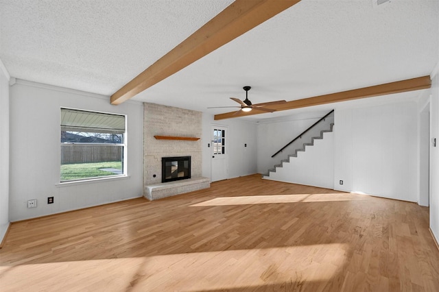 unfurnished living room featuring beam ceiling, light hardwood / wood-style flooring, a large fireplace, and a textured ceiling