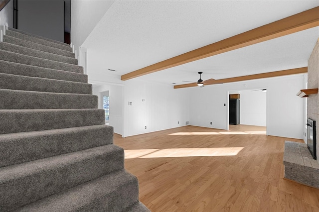 living room with a fireplace, light wood-type flooring, ceiling fan, a textured ceiling, and beam ceiling