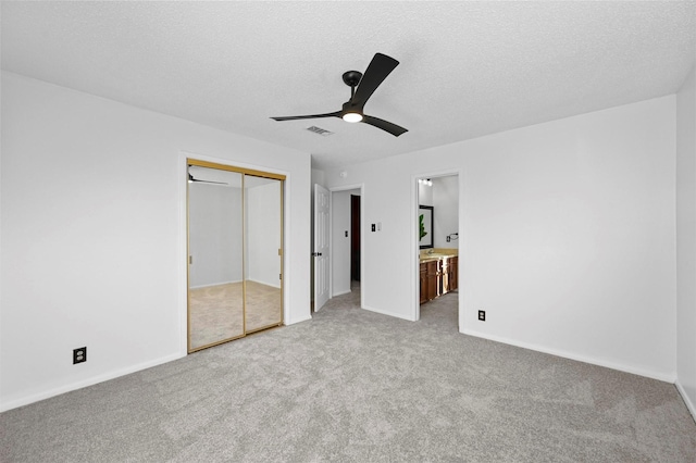 unfurnished bedroom featuring ensuite bath, light colored carpet, a textured ceiling, a closet, and ceiling fan