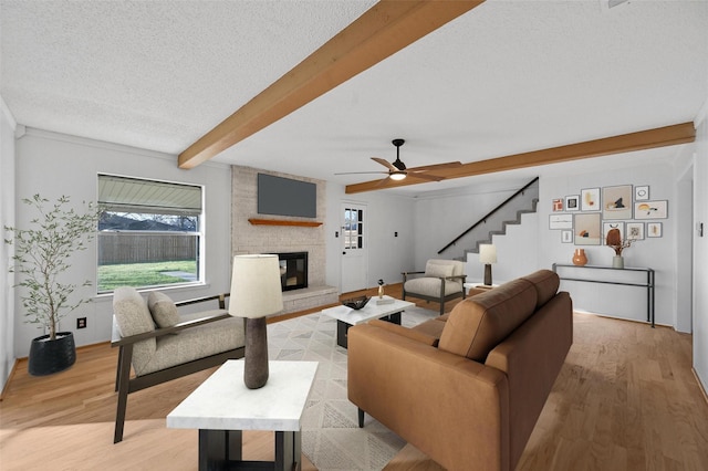 living room featuring beamed ceiling, a large fireplace, light hardwood / wood-style floors, and a textured ceiling