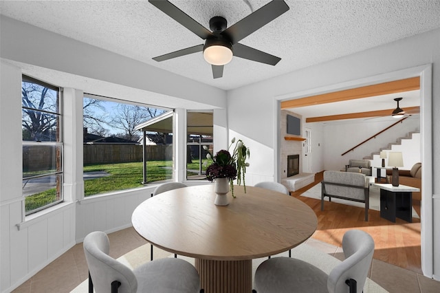 dining area with ceiling fan, a large fireplace, a textured ceiling, and light wood-type flooring