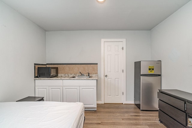 bedroom with sink, light hardwood / wood-style floors, and stainless steel refrigerator