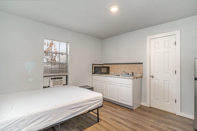 bedroom with cooling unit, light hardwood / wood-style floors, and sink