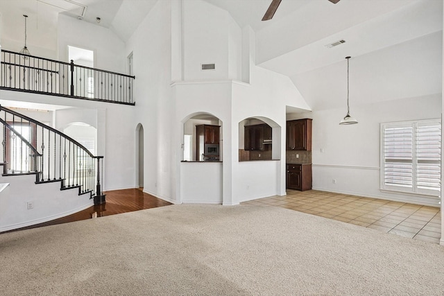 unfurnished living room featuring ceiling fan, a towering ceiling, and light colored carpet