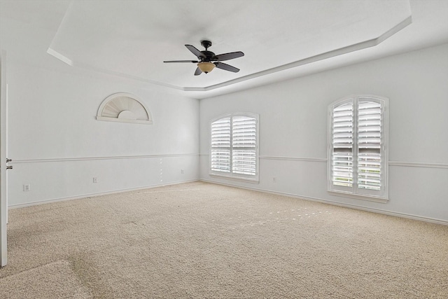 empty room with ceiling fan, a tray ceiling, and carpet floors