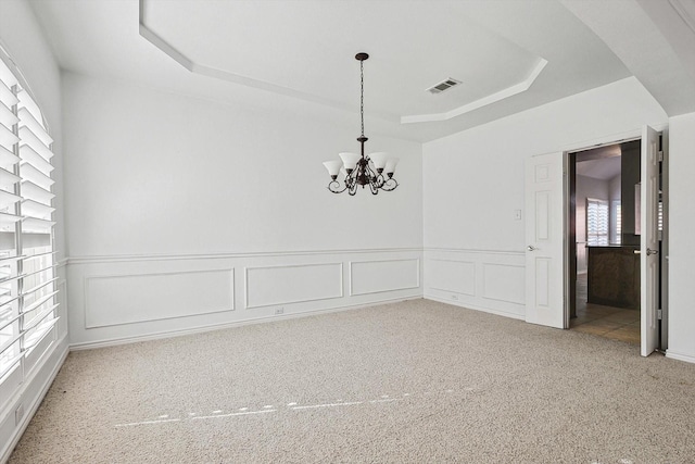 spare room with an inviting chandelier, carpet flooring, and a raised ceiling