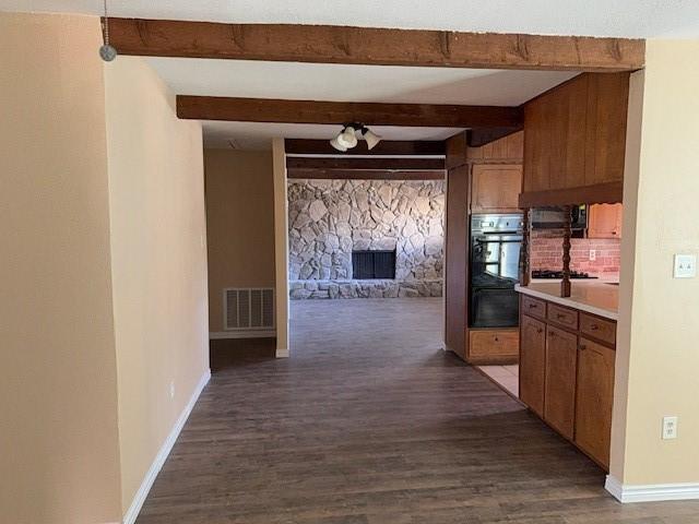 kitchen featuring beam ceiling, a stone fireplace, black double oven, and dark hardwood / wood-style floors