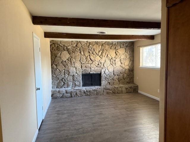 unfurnished living room featuring beam ceiling, a stone fireplace, and wood-type flooring