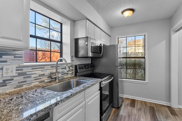 kitchen with white cabinetry, sink, light stone counters, and appliances with stainless steel finishes