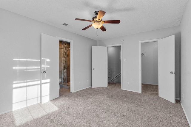 unfurnished bedroom with a walk in closet, light carpet, connected bathroom, and a textured ceiling