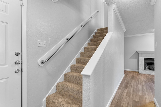 stairs with a fireplace, a textured ceiling, hardwood / wood-style flooring, and crown molding