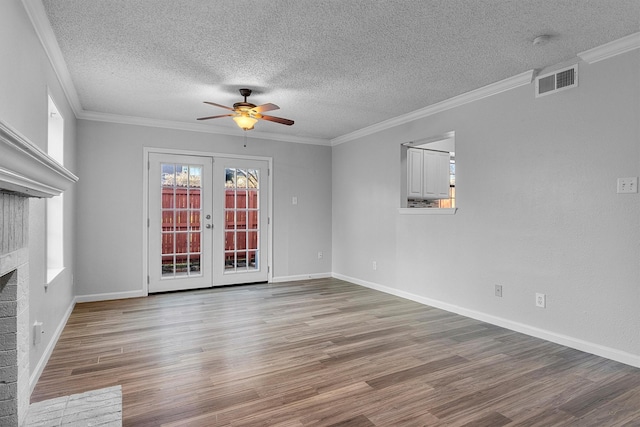 spare room featuring french doors, a brick fireplace, ornamental molding, a textured ceiling, and ceiling fan