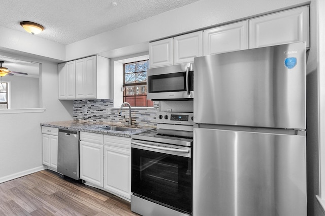 kitchen featuring sink, decorative backsplash, light stone countertops, white cabinetry, and stainless steel appliances