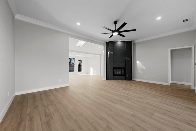 unfurnished living room featuring a skylight, ornamental molding, ceiling fan, light hardwood / wood-style flooring, and a fireplace