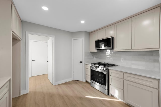 kitchen featuring tasteful backsplash, light stone countertops, light hardwood / wood-style flooring, and stainless steel appliances