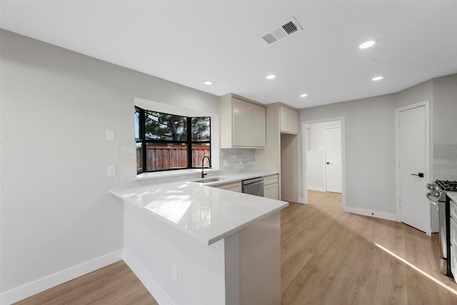 kitchen with sink, tasteful backsplash, kitchen peninsula, appliances with stainless steel finishes, and light wood-type flooring