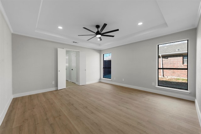 empty room with a wealth of natural light, light wood-type flooring, a tray ceiling, and ceiling fan