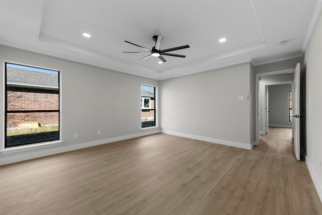 empty room with ceiling fan, light wood-type flooring, crown molding, and a tray ceiling