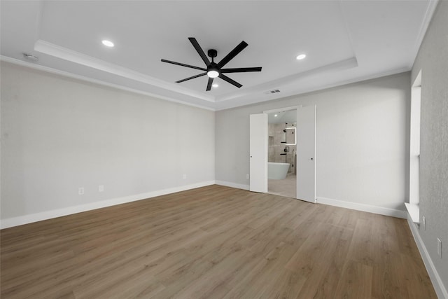 empty room featuring a tray ceiling, ceiling fan, ornamental molding, and hardwood / wood-style flooring