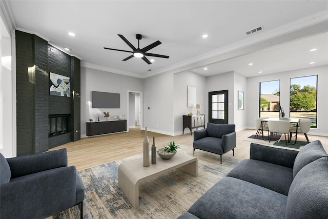 living room with ceiling fan, crown molding, a fireplace, and light hardwood / wood-style flooring