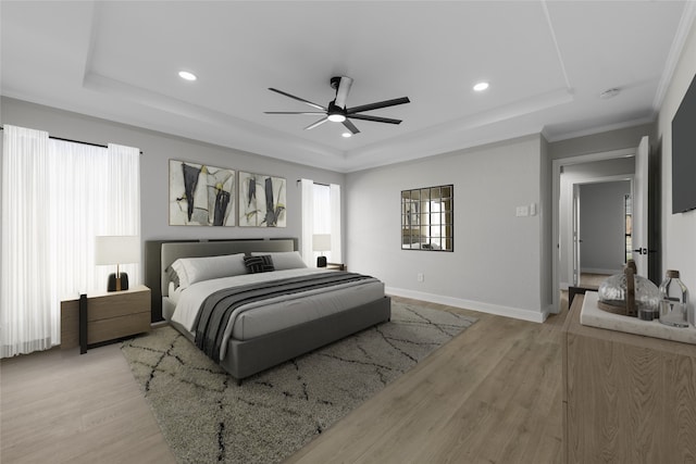 bedroom featuring a tray ceiling, ceiling fan, crown molding, and light hardwood / wood-style floors