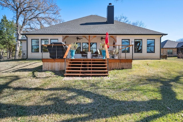 back of property with a shingled roof, a lawn, a ceiling fan, a chimney, and a deck