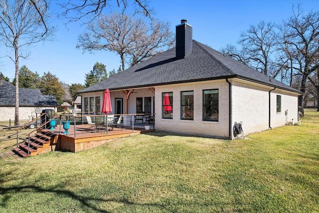 rear view of house with a chimney, roof with shingles, a deck, a yard, and brick siding