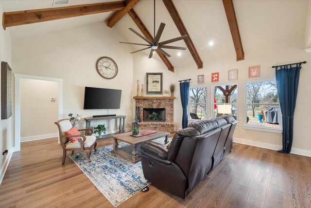 living area featuring high vaulted ceiling, beamed ceiling, a brick fireplace, and wood finished floors