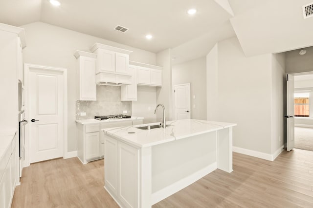 kitchen featuring light wood finished floors, stainless steel appliances, visible vents, a sink, and an island with sink