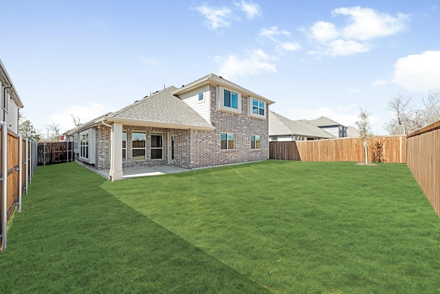 back of property with a fenced backyard, brick siding, roof with shingles, a lawn, and a patio area